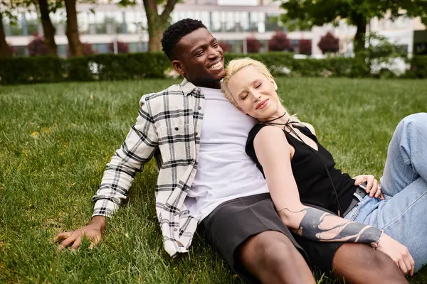 A multicultural couple, an African American man, and a Caucasian woman, sitting happily together in the lush green grass of a park.