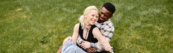 A multicultural couple, an African American man and Caucasian woman, sitting together contently in the lush green grass of a park.