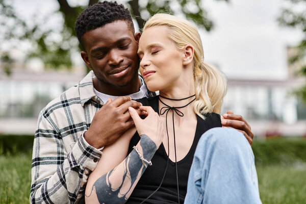 Мультикультурная пара, афроамериканец и кавказка, наслаждаются мирным моментом, сидя вместе в пышной зеленой траве парка.