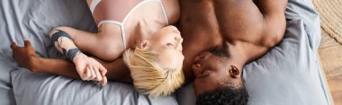 A multicultural couple lying on a bed, exuding sensuality and comfort in each others embrace. clipart