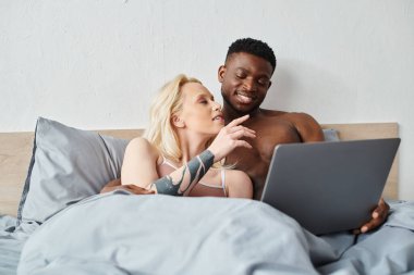 Çok kültürlü bir çift, dizüstü bilgisayarlarının içeriğine dalmış bir şekilde yatakta dinleniyor..