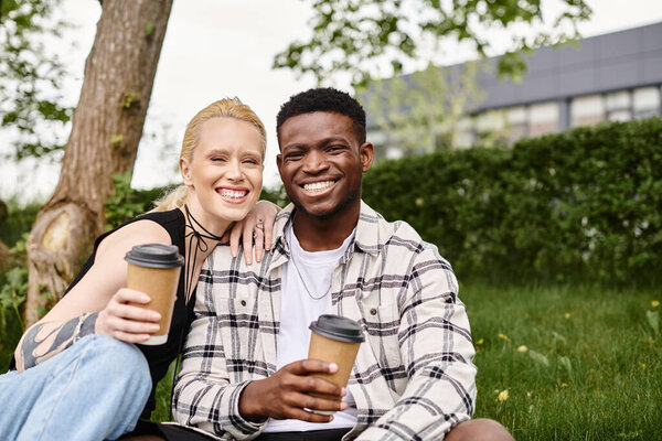 Multicultural couple, an African American man and a Caucasian woman, enjoying coffee together while seated on grass.