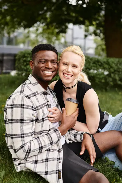 Multicultural couple, an African American man, and a Caucasian woman sitting together on the grass in a park, enjoying the moment.