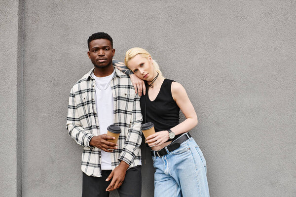 A happy, multicultural couple standing together on an urban street near a grey building.
