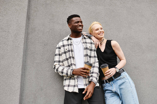 A multicultural couple, a man and a woman, standing happily together on an urban street by a grey building.