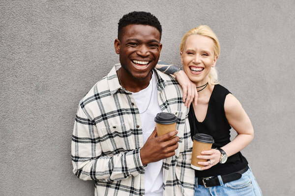 A multicultural couple enjoys a coffee break on an urban street, with the man standing next to the woman holding a cup of coffee.