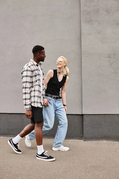 stock image A happy multicultural couple, boyfriend and girlfriend, walking together on an urban street near a grey building.