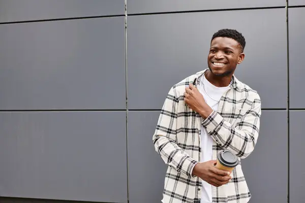 stock image happy black man standing in front of a gray urban wall, exuding happiness.