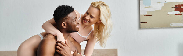 A sexy, multicultural couple sitting close on a bed in a cozy home setting.