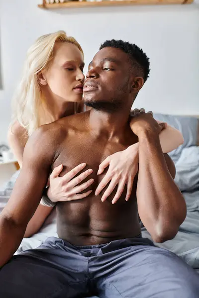 Stock image A multicultural boyfriend and girlfriend sit together on a bed, sharing a moment of peaceful intimacy.