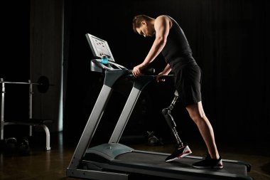 Protez bacaklı bir adam karanlık spor salonunda koşu bandında çalışıyor.