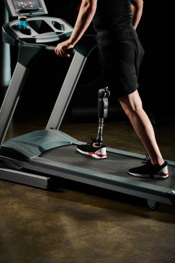 Protez bacaklı engelli bir adam spor salonunda koşu bandında yürüyor..
