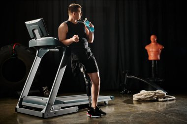 A man with a prosthetic leg stands on a treadmill, holding a bottle of water. clipart