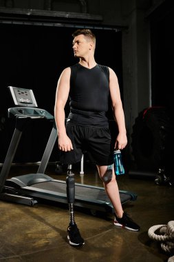 Protez bacaklı engelli bir adam spor salonundaki koşu bandında duruyor. Kararlı ve antrenmanına odaklanmış..