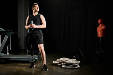 Protez bacaklı bir adam spor aletlerinin önünde kendine güvenerek duruyor. Spor yaparken kararlılık ve dayanıklılık gösteriyor..