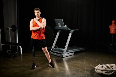 Protez bacaklı bir adam koşu bandının önünde duruyor. Spor salonunda antrenman yapmaya hazır..