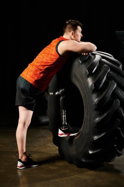 A man with a prosthetic leg stands next to a massive tire, ready to embark on a challenging workout routine. clipart