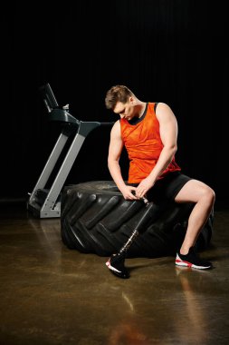 Spor salonunda siyah bir lastiğin tepesinde oturan protez bacaklı bir adam spor yaparken güç ve kararlılık gösteriyor..