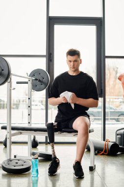 Protez bacaklı bir adam spor salonundaki bir bankta oturur, dinlenmek ve antrenman sırasında düşünmek için zaman ayırır..