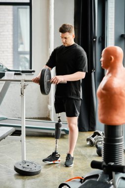 Protez bacaklı engelli bir adam modern bir odada bir spor makinesinin yanında duruyor..
