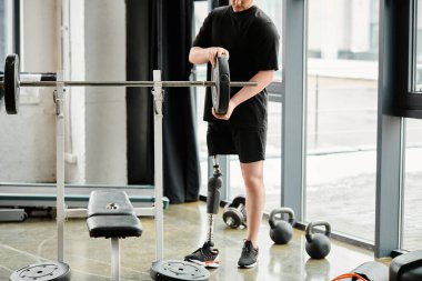 Protez bacaklı engelli bir adam spor salonunda elinde bir çubukla duruyor. Güç ve dayanıklılık kazanmak için çalışıyor..