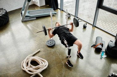 Protez bacaklı bir adam spor salonunda güçlü bir kaldırıcıya bağlanır. Güç ve kararlılık gösterir..