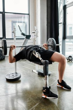 Protez bacaklı bir adam spor salonunda ağırlık kaldırırken halter kaldırıyor..