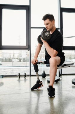 Protez bacaklı bir adam elinde bir su ısıtıcısı olan bir bankta oturur ve spor salonundaki antrenman rutinine odaklanır..