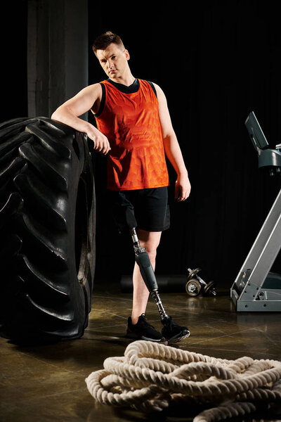 A man with a prosthetic leg stands next to a large tire, showcasing strength and determination in the gym.