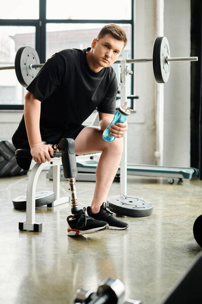A man with a prosthetic leg, sits on a bench, holding a bottle of water.