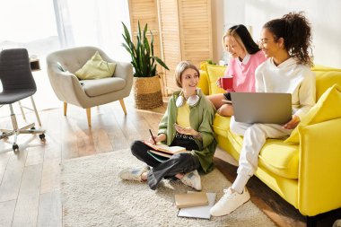 Bir grup kadın, açık sarı bir kanepede oturup birlikte ders çalışıyor ve dostluk anlarını paylaşıyor..