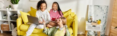 A group of interracial teenage girls sit on a bright yellow chair, studying together at home, fostering friendship and education. clipart