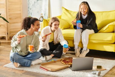 Farklı ırktan üç genç kız yerde oturup sıcak bir ortamda pizza ve kahvenin tadını çıkarıyorlar..