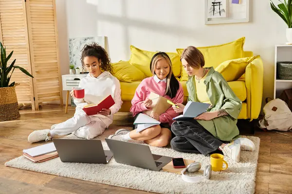 stock image Three teenage girls of different races are seated on the floor, engrossed in their laptops, working on a project together.