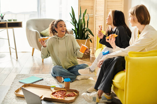 Multicultural teenage girls gather in a cozy living room, bonding over slices of pizza and sharing laughter.