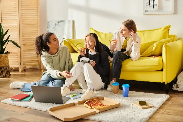 Stock image A group of diverse teenage girls chatting and laughing while sitting on the floor next to a vibrant yellow couch in a cozy home setting.