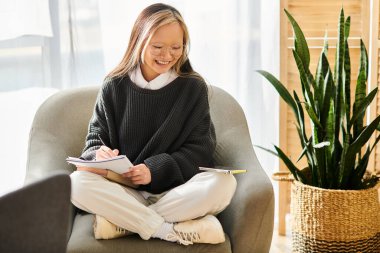 Genç Asyalı bir kadın, evinde bir sandalyede otururken kendini kitaba kaptırmış.