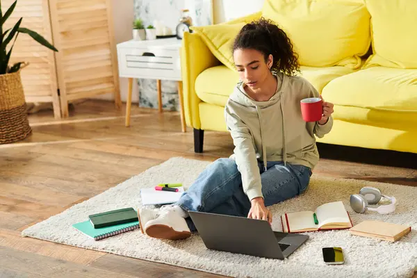 一个少女坐在地板上 专心致志地在笔记本电脑上学习 同时还喝了一杯咖啡 — 图库照片