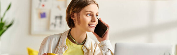 A focused teenage girl sits at a desk, conversing on a cell phone while using a laptop for e-learning at home.
