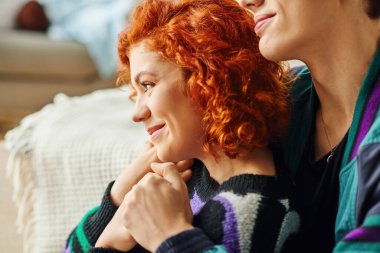 Keyifli, modaya uygun, rahat elbiseli çiftimiz evlerinde sevgi dolu bir şekilde oturup birbirlerine sarılıyorlar.