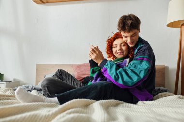 Kulaklıklı, neşeli, yakışıklı bir adam. Evde, yatakta sevgilisine sevgiyle sarılıyor.