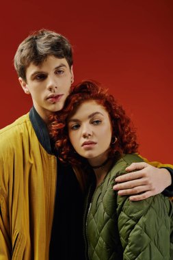 Çekici kızıl saçlı kadın. Yakışıklı sevgilisiyle poz veriyor. Kırmızı renkli arka planda.