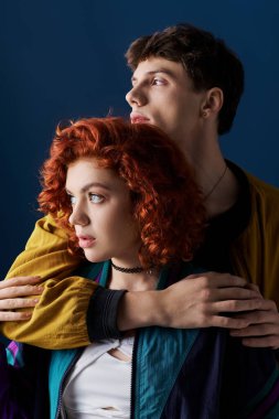 Havalı gündelik giysiler içinde çekici bir çift sarılıyor ve mavi arka plana bakıyor.