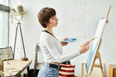 A woman in a white shirt paints on an easel. clipart