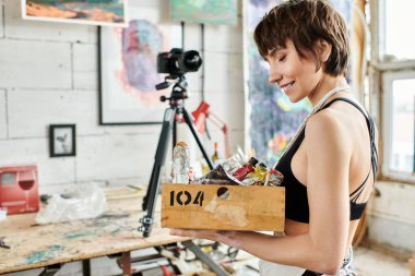 Woman showcases box of paint in front of camera. clipart