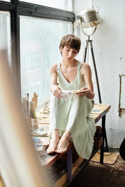 Bir kadın pencerenin önündeki masaya oturur ve derin derin dışarı bakar..