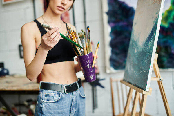 A woman gracefully holding a cup of paint and a brush.