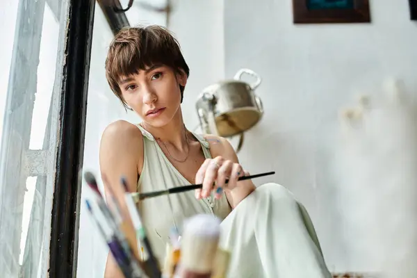 stock image Appealing woman sits on a window sill, holding a brush.