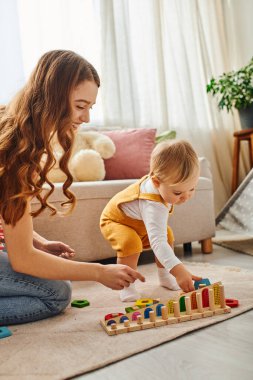 Genç bir anne, yeni yürümeye başlayan kızıyla rahat evlerinde yerde oynayarak mutlu olur..
