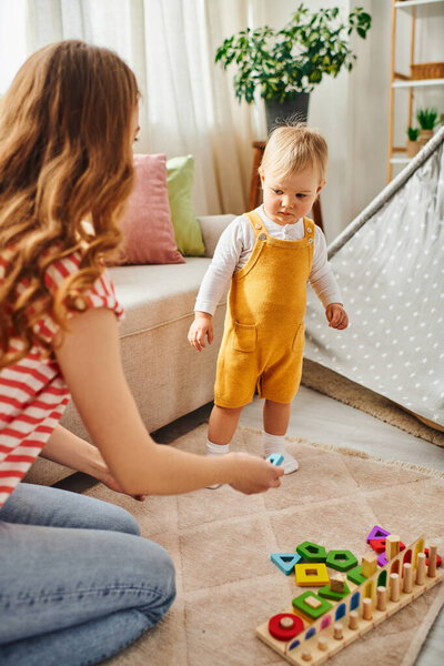A young mother affectionately plays with her baby daughter on the cozy floor of their home.